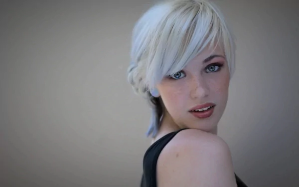 HD desktop wallpaper featuring a woman with platinum blonde hair and striking blue eyes, tagged with Devon Jade. She looks over her shoulder against a blurred background.