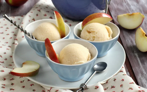 HD desktop wallpaper of three bowls of ice cream garnished with apple slices, set on a plate with a spoon, placed on a tablecloth.