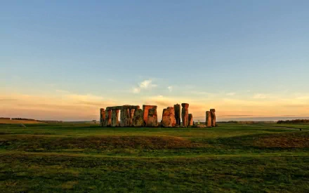 HD desktop wallpaper featuring Stonehenge, the iconic man-made stone monument set against a serene sunset sky and expansive green landscape.