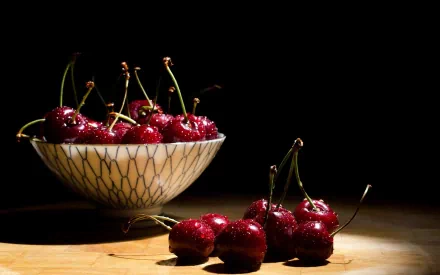 A vibrant display of fresh cherries in a patterned bowl, illuminated against a dark background, creating an appealing HD desktop wallpaper.