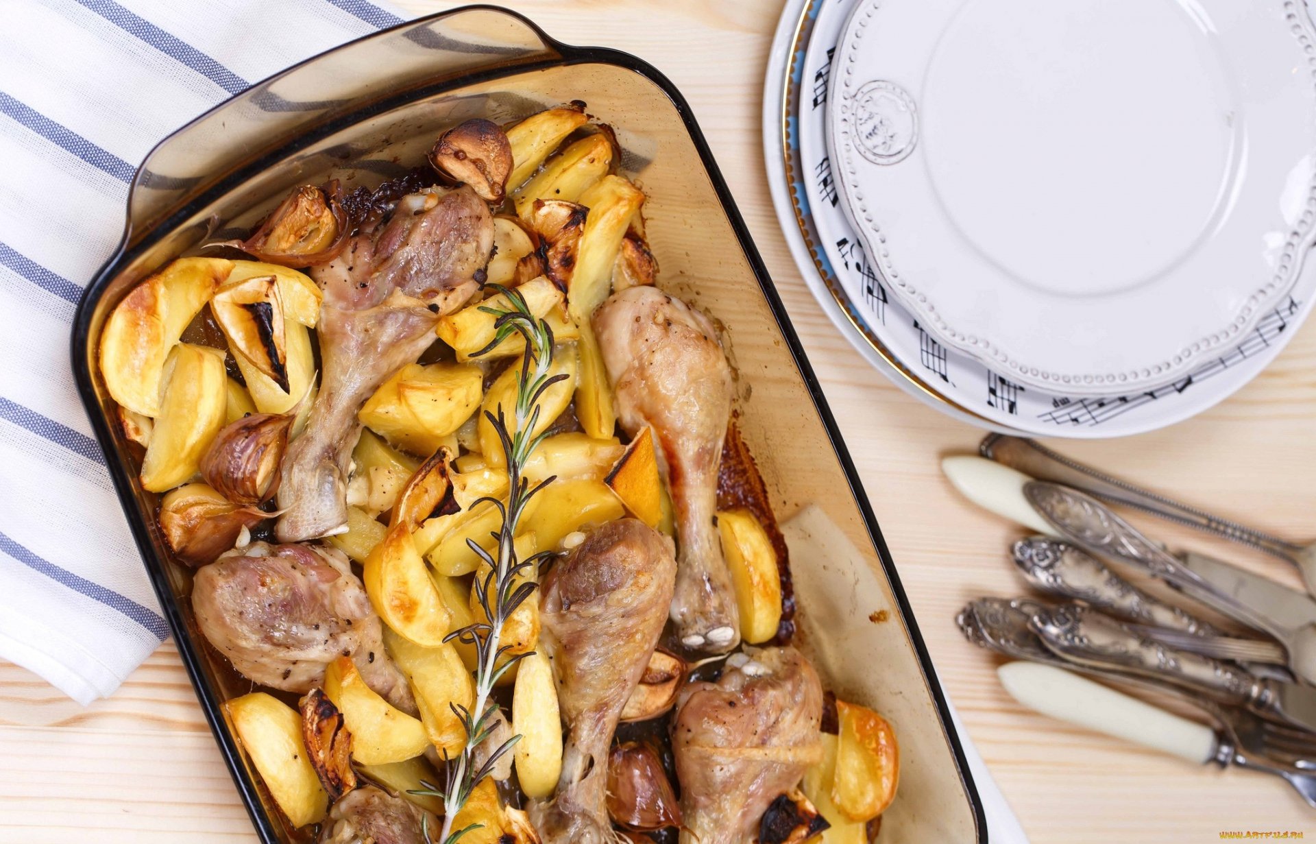 HD desktop wallpaper featuring a roasted meat and potato dish in a glass baking tray, accompanied by plates and cutlery on a striped cloth.