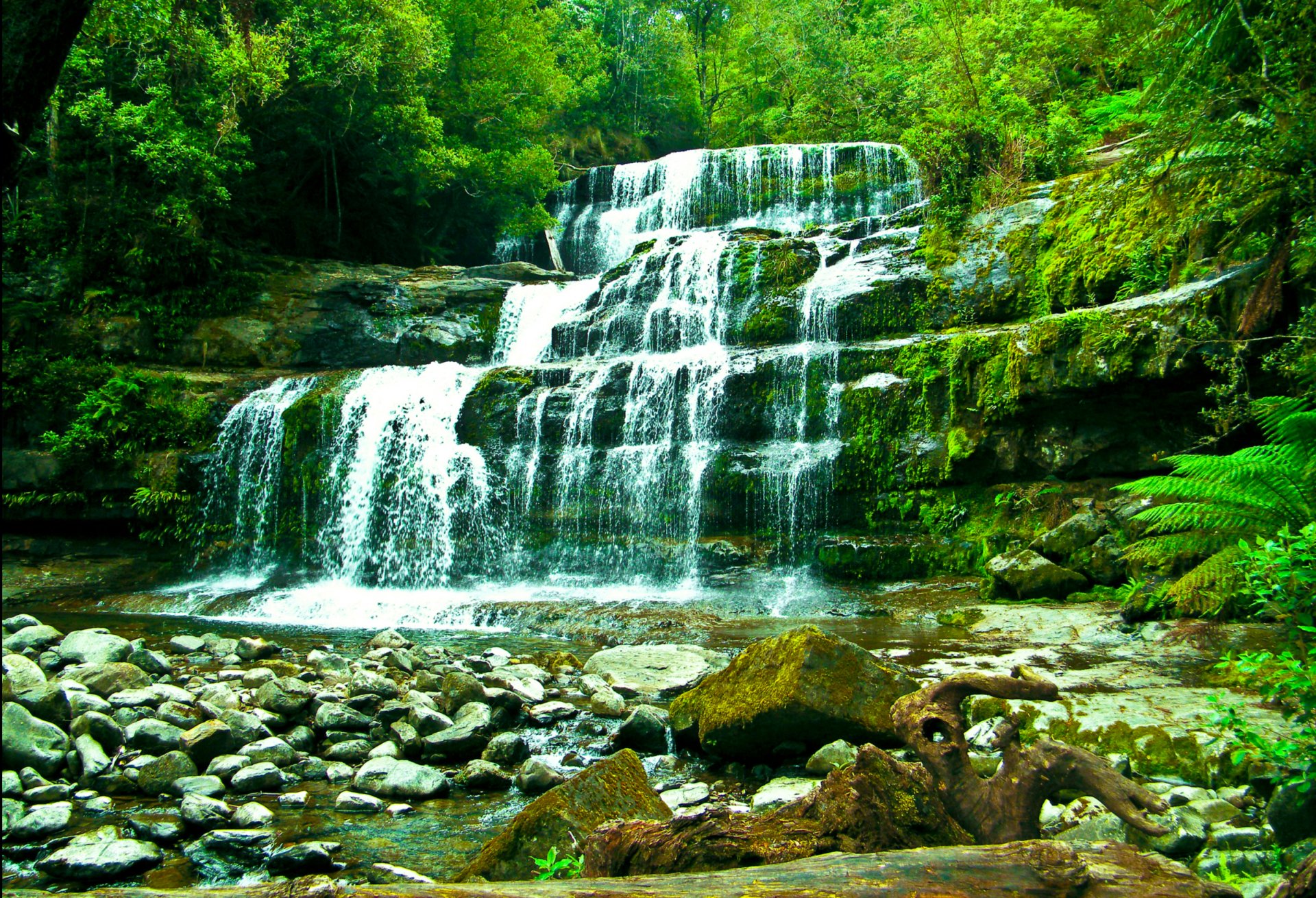 HD PC desktop wallpaper featuring a serene waterfall cascading through lush green forest surrounded by rocks and foliage in a vibrant nature scene.