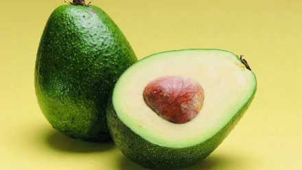 A vibrant HD desktop wallpaper featuring a halved avocado, showcasing its creamy texture and seed on a bright yellow background, emphasizing its fresh and appealing look.