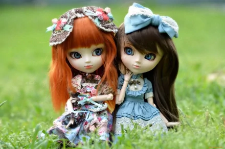 Two intricately designed dolls with vibrant hair and stylish outfits sit together on lush green grass, creating a charming and whimsical scene for a high-definition desktop wallpaper.