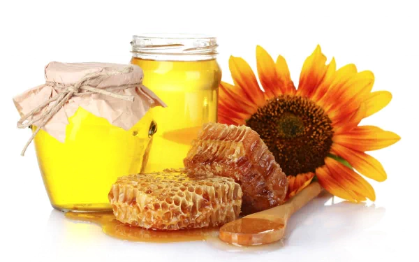 HD desktop wallpaper featuring jars of golden honey, honeycomb pieces, a wooden spoon, and a vibrant sunflower arranged on a white background.