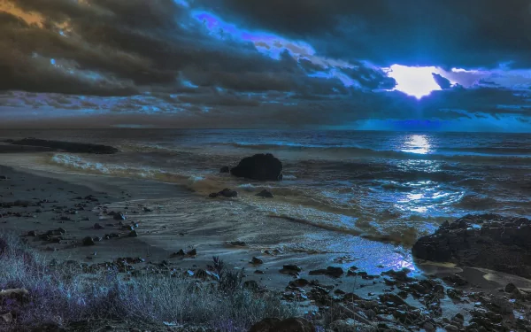 4K Ultra HD PC desktop wallpaper showing a dramatic beach scene with dark clouds, rugged rocks, and moonlight reflecting on the ocean waves at night.