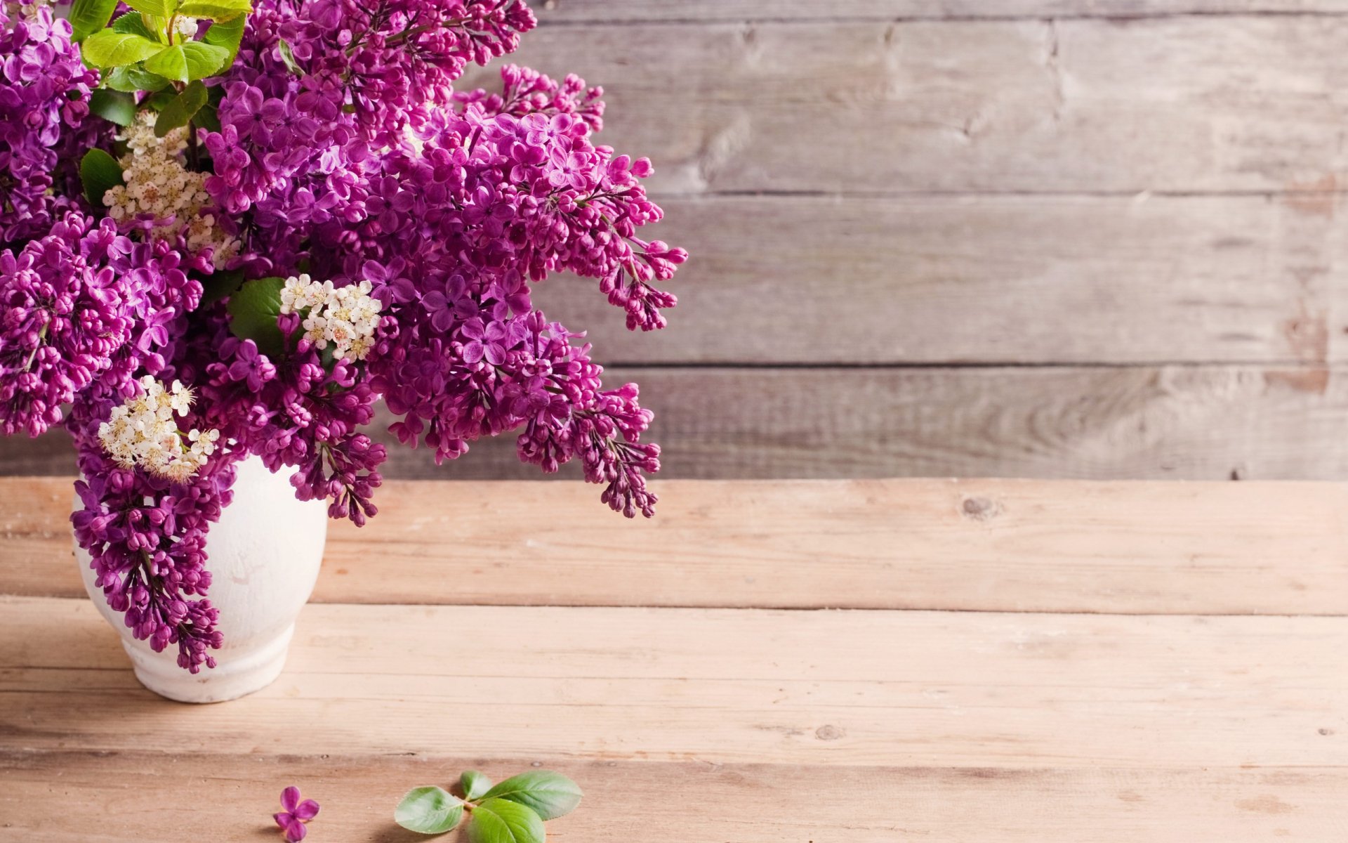 HD PC desktop wallpaper featuring a vibrant bouquet of man-made purple flowers in a white vase on a light wooden table against a rustic wooden backdrop.