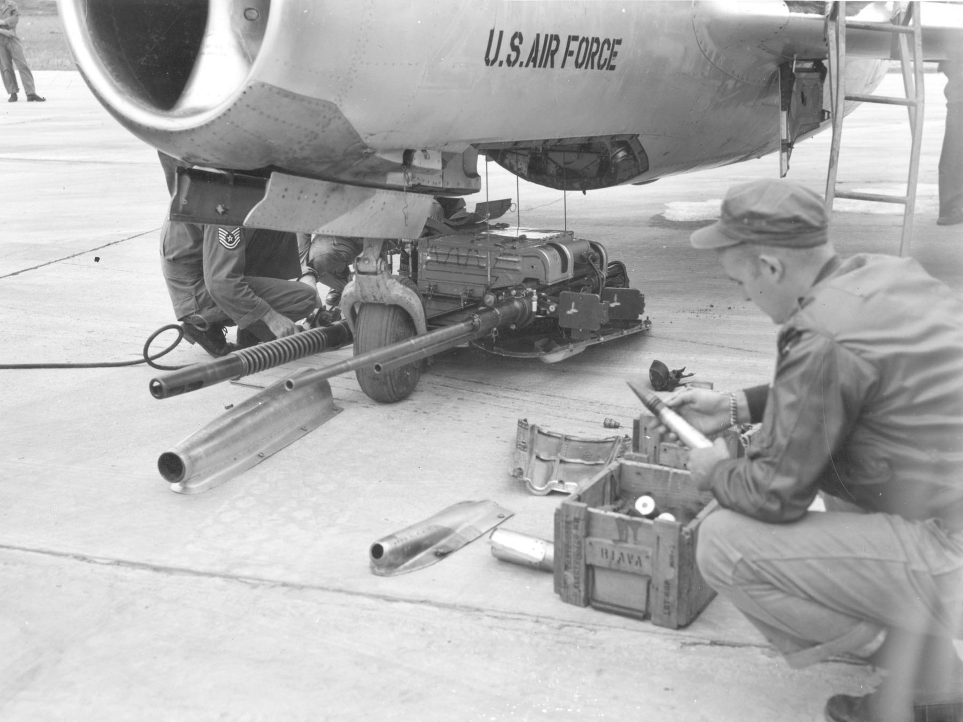 Black and white HD PC desktop wallpaper showing military personnel servicing aircraft weaponry on the ground.