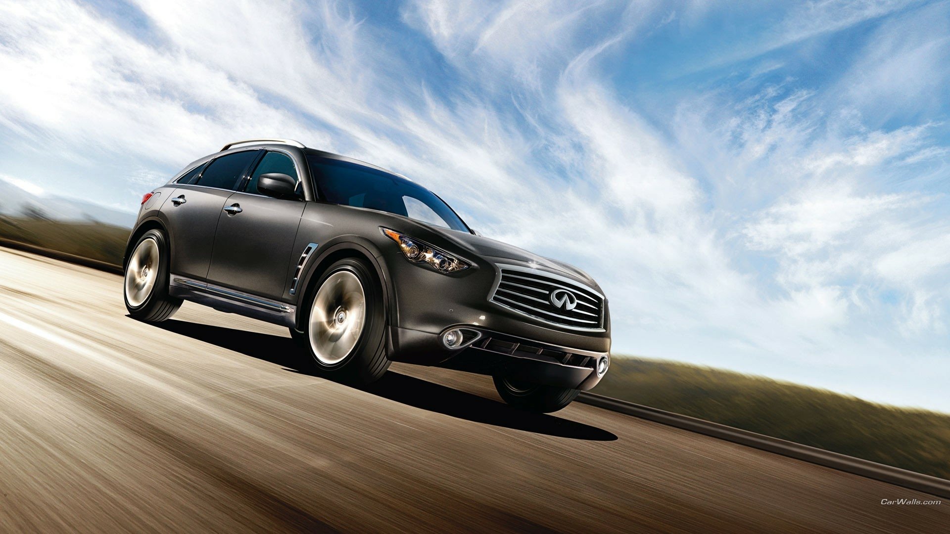 HD PC desktop wallpaper background of an Infiniti QX70 vehicle speeding along a sunlit open road beneath sweeping blue and white skies.