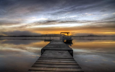 HD desktop wallpaper of a man-made wooden pier extending into calm water under a dramatic, cloudy sky at sunset.