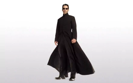 Neo from The Matrix, portrayed by Keanu Reeves, stands confidently in a long black coat and sunglasses, set against a minimalist white background in this HD wallpaper.