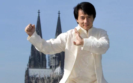HD wallpaper featuring celebrity Jackie Chan in a martial arts pose, with a majestic gothic cathedral in the background on a clear day.