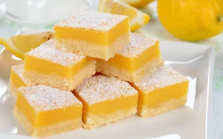 A delicious stack of lemon bars dusted with powdered sugar, set against fresh lemons. This HD desktop wallpaper captures the vibrant colors and textures of this delightful treat.
