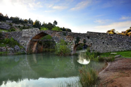 HD desktop wallpaper featuring a man-made stone bridge arching over calm water, surrounded by greenery and a clear sky in a natural setting.
