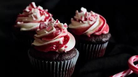 HD desktop wallpaper featuring a close-up of rich chocolate cupcakes topped with swirling red and white frosting, set against a dark background.