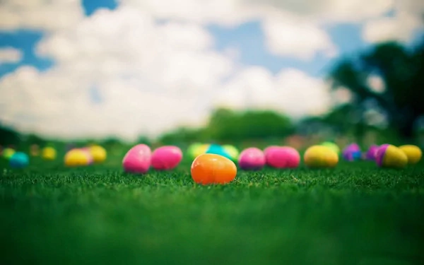 Colorful Easter eggs scattered across vibrant green grass under a bright sky, creating a cheerful holiday atmosphere. Use as an HD desktop wallpaper or background.
