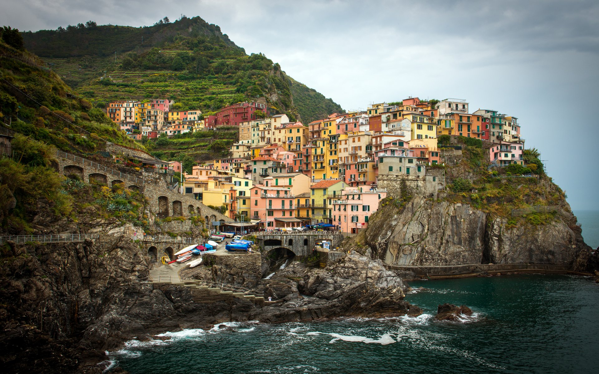 HD desktop wallpaper showcasing the colorful, man-made village of Manarola perched on cliffs by the sea under a cloudy sky.