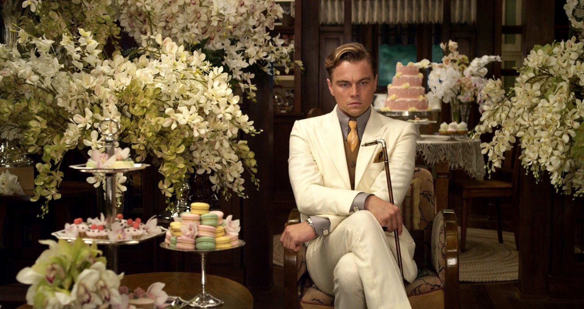 HD wallpaper of Leonardo DiCaprio as Gatsby, seated amidst lavish decor and flowers from The Great Gatsby film.