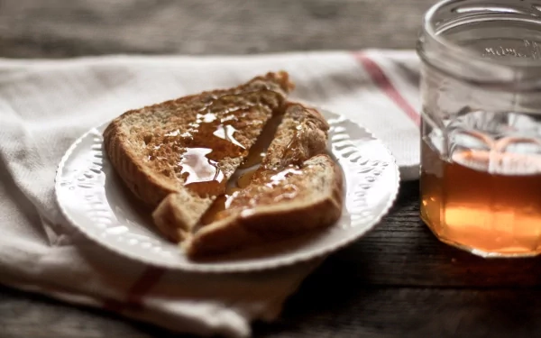 HD food-themed PC wallpaper showing toasted bread drizzled with honey on a plate, accompanied by a glass jar of honey on a rustic wooden table.