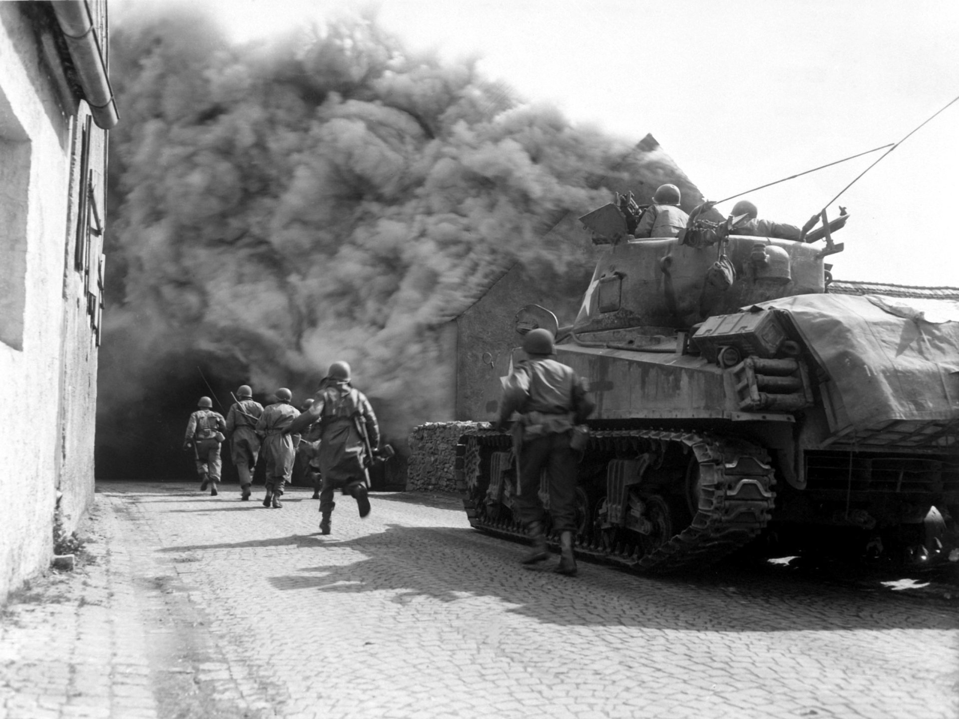HD desktop wallpaper of a military scene featuring soldiers advancing alongside a tank with smoke billowing in the background during combat.