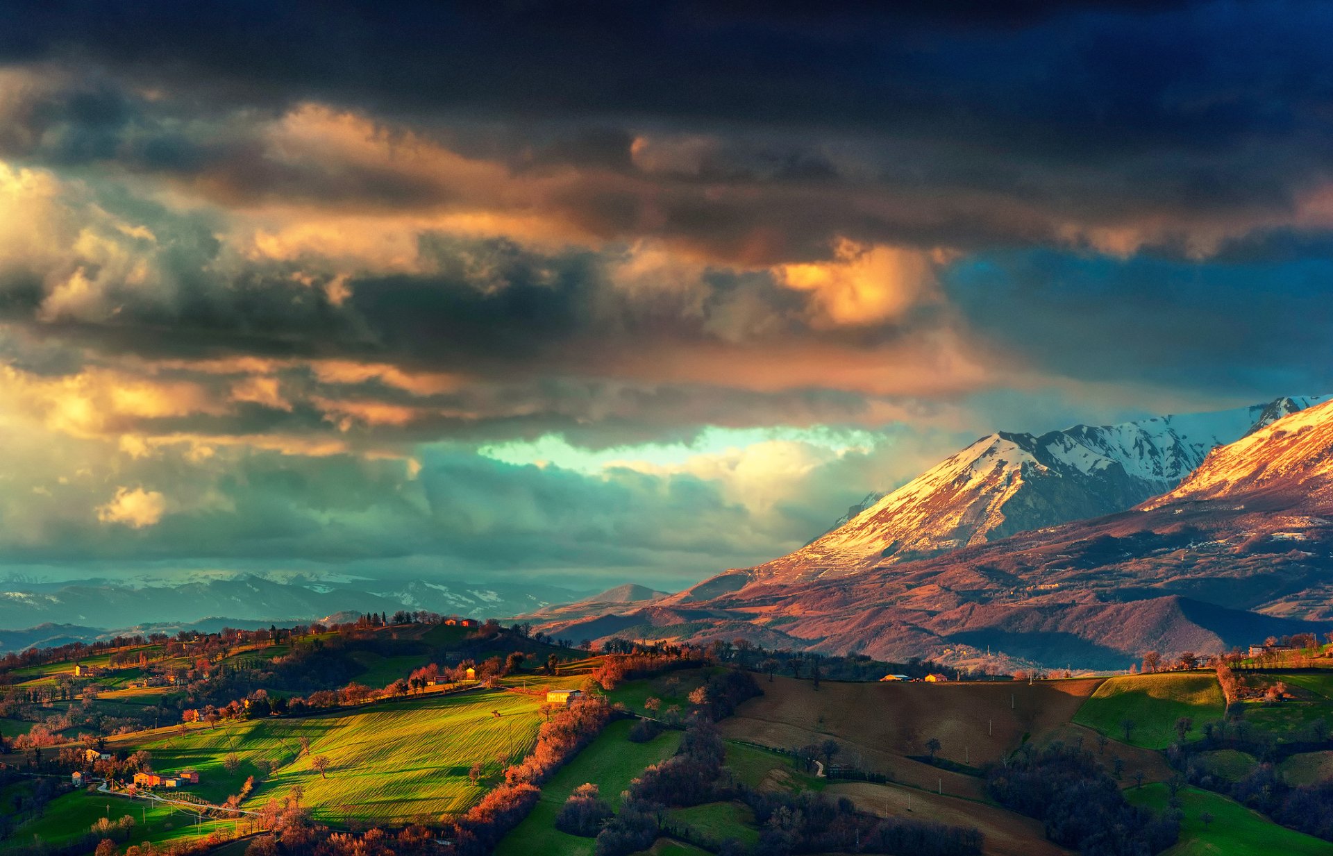 HD desktop wallpaper depicting a dramatic landscape with snow-capped mountains and lush green fields under a vibrant, cloud-filled sky.