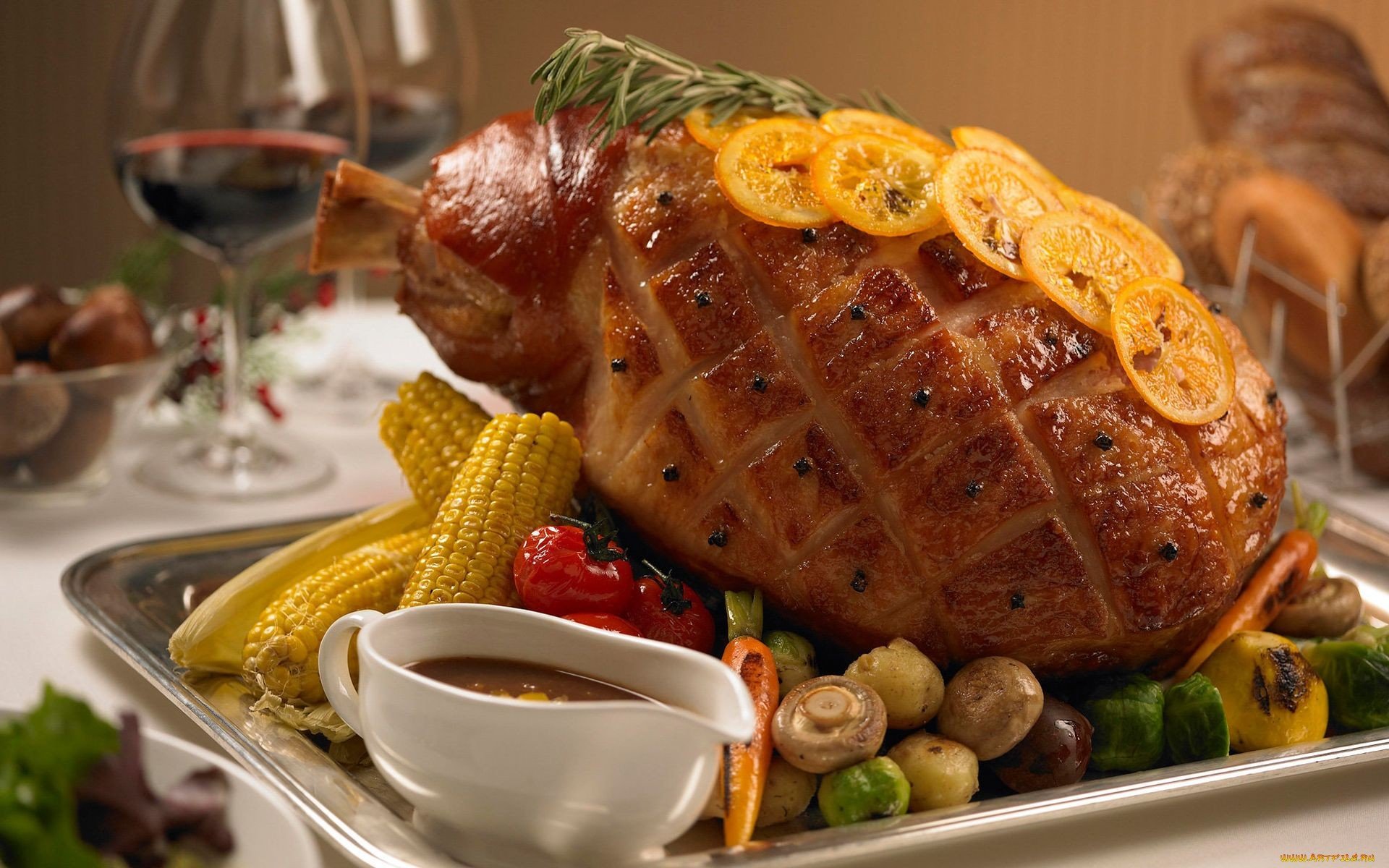 HD desktop wallpaper showcasing a roasted ham garnished with orange slices, surrounded by corn, mushrooms, peppers, and a gravy boat, set on a festive dining table.