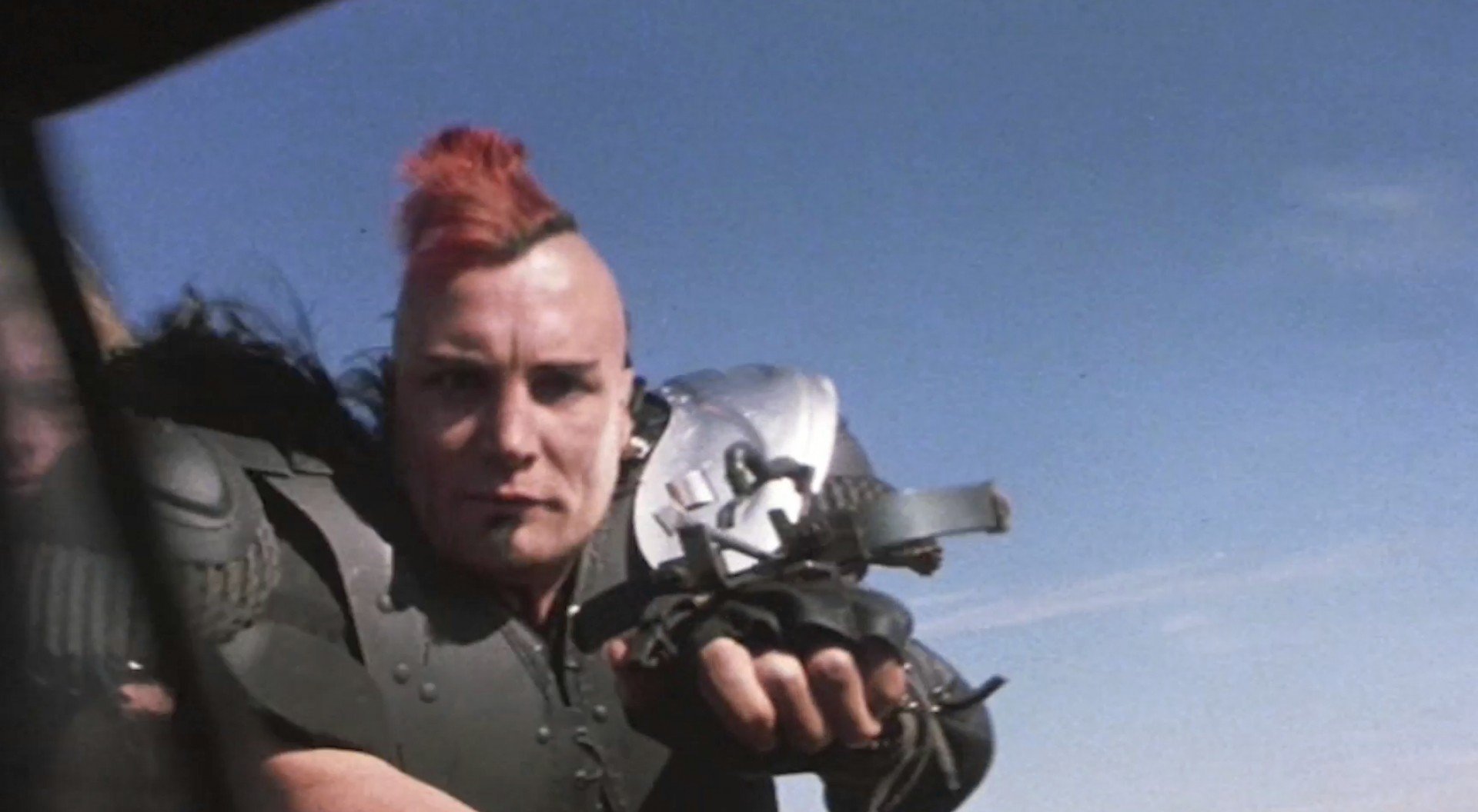 Close-up of an armored punk warrior from the Mad Max movie reaching out with a gloved hand against a clear blue sky — HD PC desktop wallpaper/background.