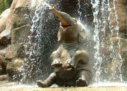 HD desktop wallpaper of a joyful Asian elephant bathing under a waterfall, raising its trunk amidst splashing water.