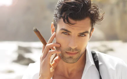 A stylish man poses with a cigar, exuding confidence, set against a serene beach backdrop. This high-definition image serves as an engaging desktop wallpaper.
