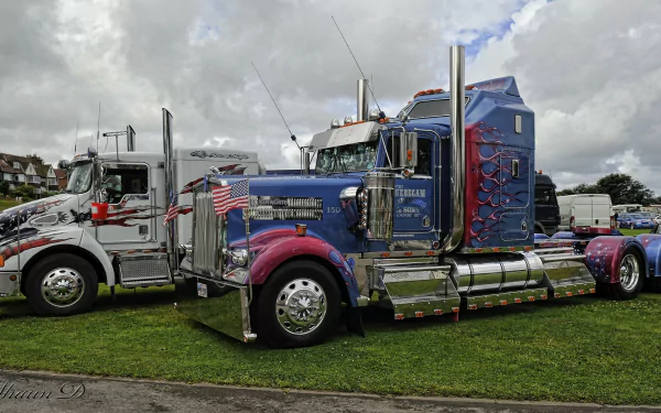 A striking Kenworth truck with vibrant colors and decorative details parked on grass, showcasing its impressive design beside another vehicle under a partly cloudy sky.