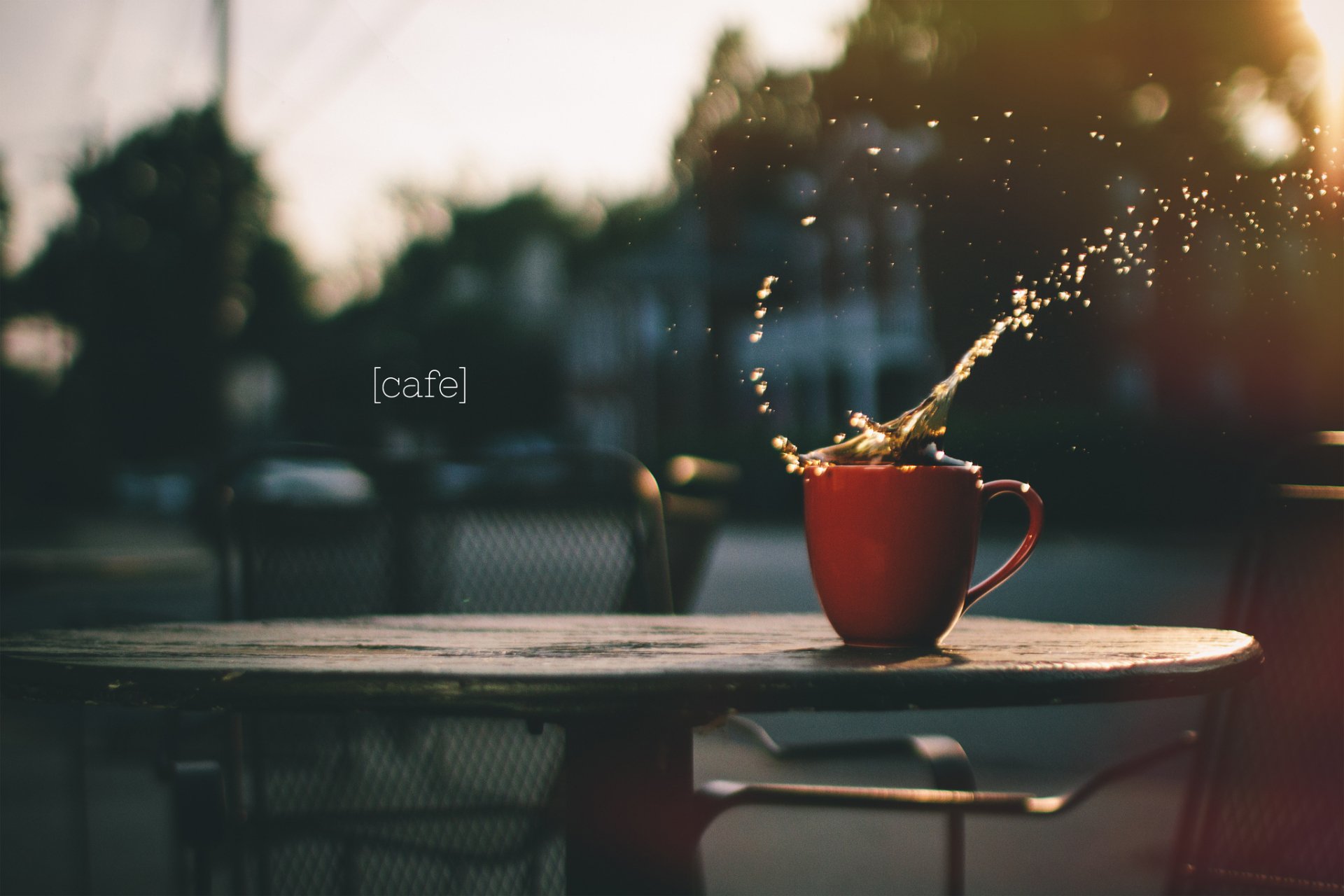 HD PC desktop wallpaper showing a red coffee cup splashing on an outdoor café table with a blurred background and warm sunlight.