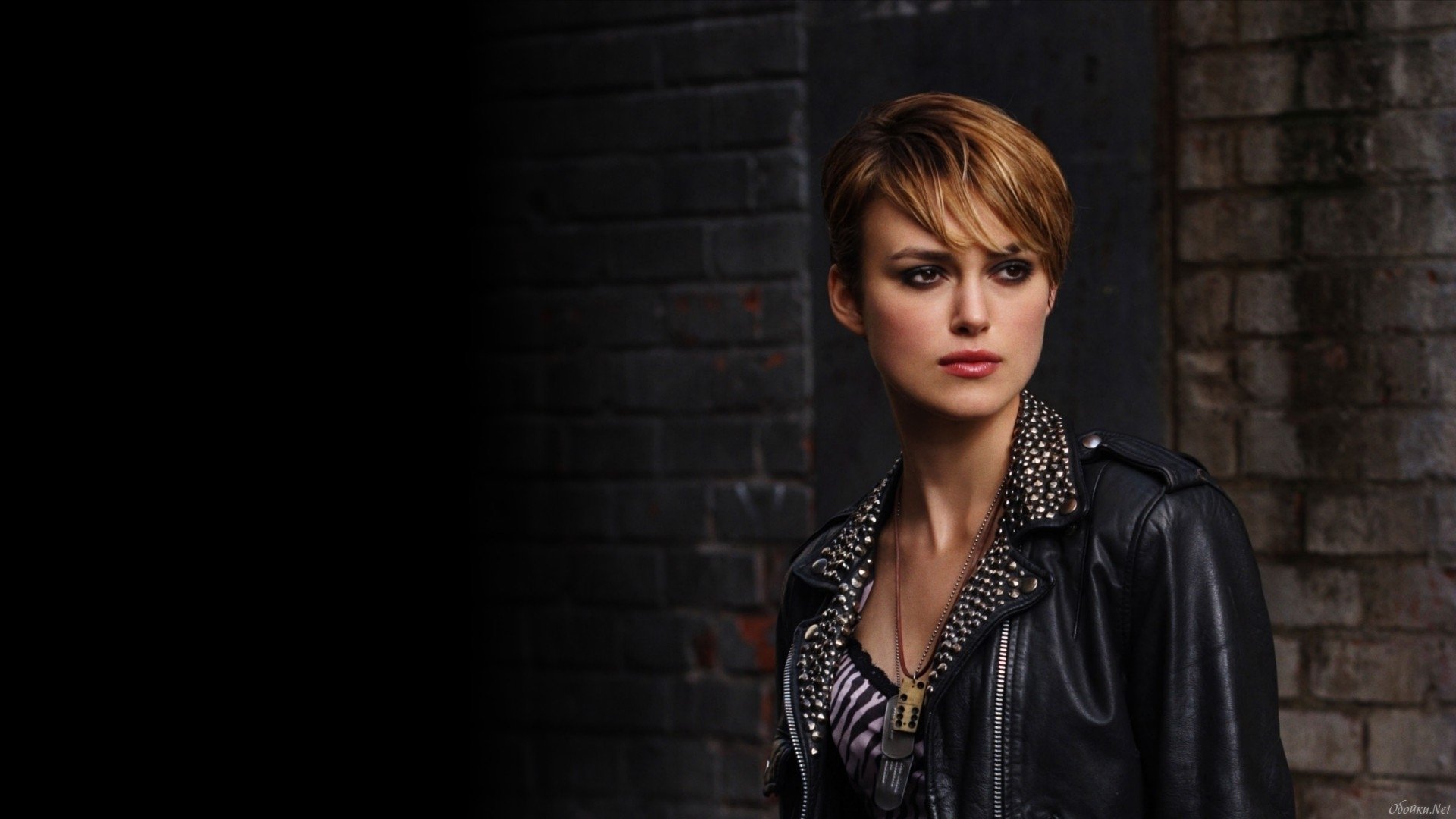 A striking HD wallpaper featuring Keira Knightley, showcasing her in a stylish leather jacket against a dark, textured background, exuding confidence and elegance.