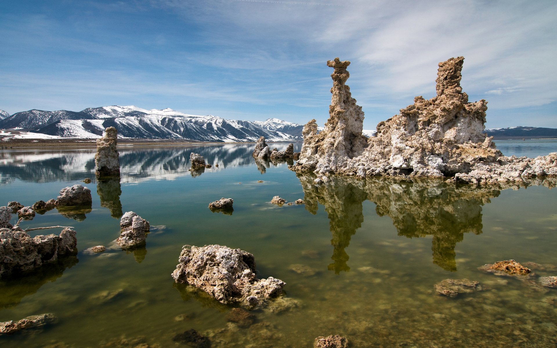 HD PC desktop wallpaper showcasing a serene nature scene with rocky formations reflected in calm waters against a backdrop of snow-capped mountains under a clear sky.