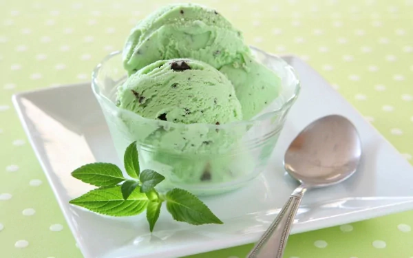 HD desktop wallpaper of mint ice cream in a clear bowl with fresh mint leaves and a spoon, set on a green polka-dotted background.