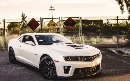 A sleek white Chevrolet Camaro parked against a backdrop of warning signs and industrial fencing, captured in high-definition as a desktop wallpaper.