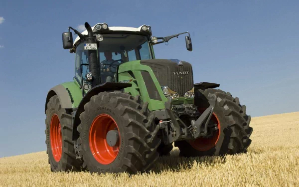 A Fendt tractor with distinctive green and orange tires stands prominently in a golden field under a clear blue sky, serving as a striking HD PC desktop wallpaper and background.