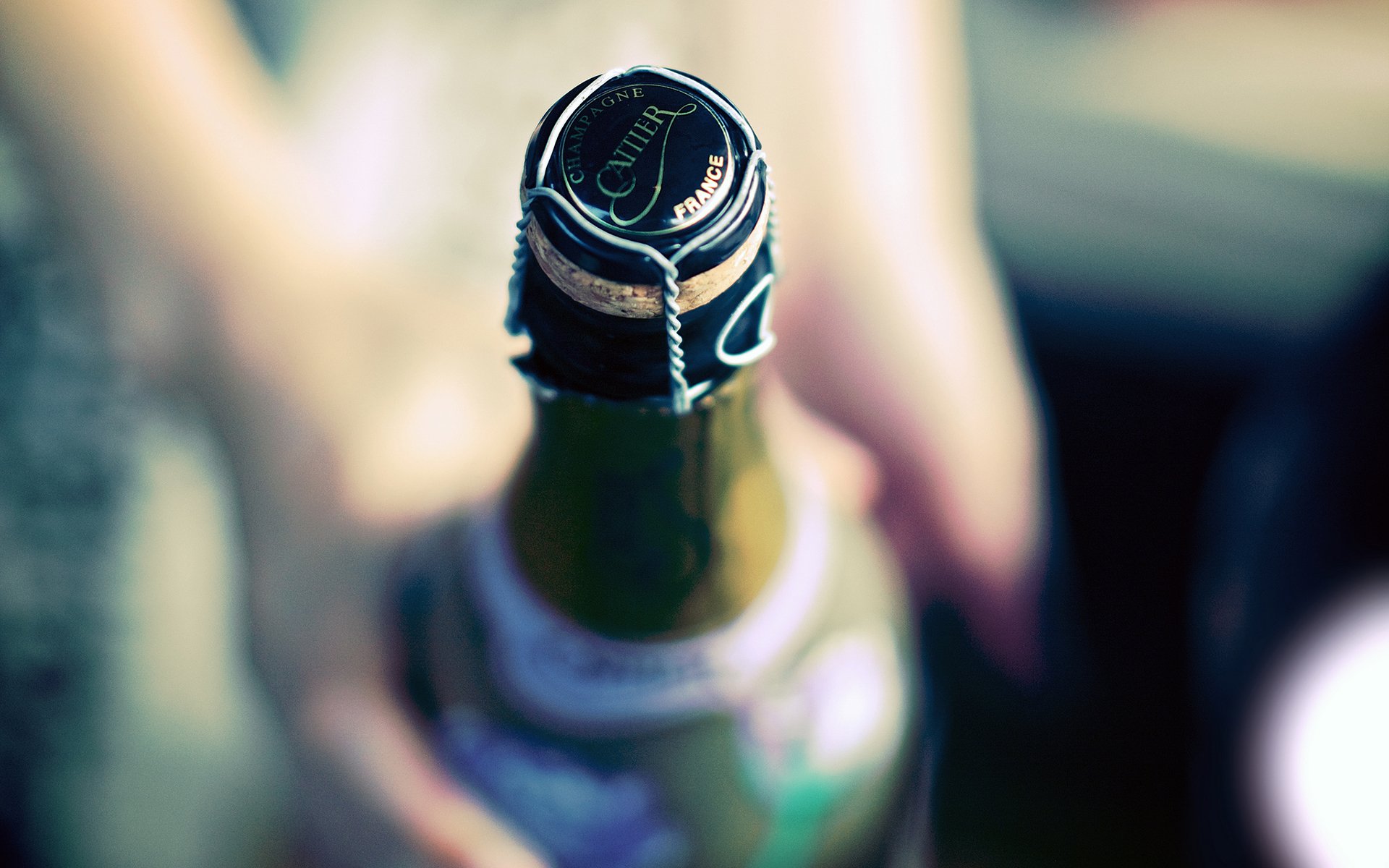 HD PC desktop wallpaper and background: close-up of a champagne bottle top with wire cage and foil, blurred hand in soft-focus background, food/champagne theme.