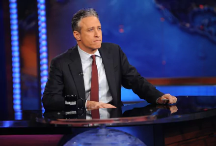 HD desktop wallpaper of a man seated at a desk on the set of The Daily Show with Jon Stewart.