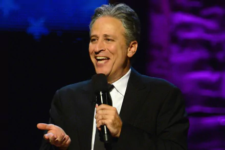 HD wallpaper featuring the host of The Daily Show with Jon Stewart, smiling while holding a microphone.