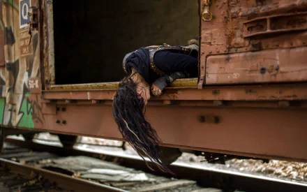 A woman with long hair leans out of a weathered train car, capturing a moody atmosphere. This HD wallpaper adds an intriguing touch to any desktop background.