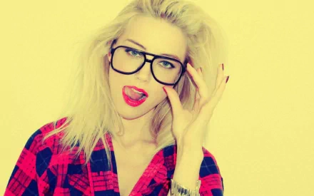 HD desktop wallpaper featuring a celebrity with blonde hair and glasses, playfully posing against a light yellow backdrop while wearing a red plaid shirt.