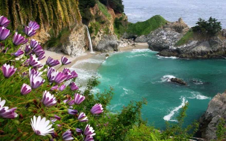 A stunning view of McWay Falls cascading into a turquoise cove, framed by lush greenery and vibrant flowers, showcasing the beauty of nature along the coastline.
