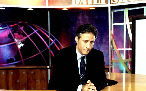 HD desktop wallpaper featuring Jon Stewart on the set of The Daily Show, presenting a thoughtful expression against a vibrant background with a globe motif.