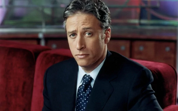 HD wallpaper featuring the host from The Daily Show with Jon Stewart in a suit, poised against a plush red backdrop.