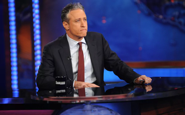 HD desktop wallpaper of a man seated at a desk on the set of The Daily Show with Jon Stewart.