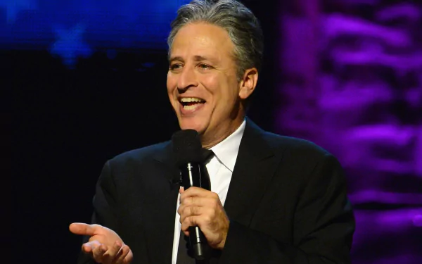 HD wallpaper featuring the host of The Daily Show with Jon Stewart, smiling while holding a microphone.