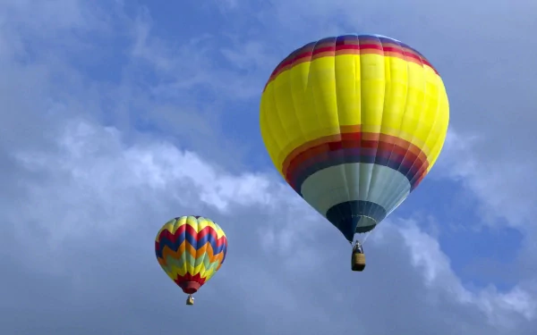 HD desktop wallpaper featuring two colorful hot air balloons floating against a bright blue sky with scattered clouds.