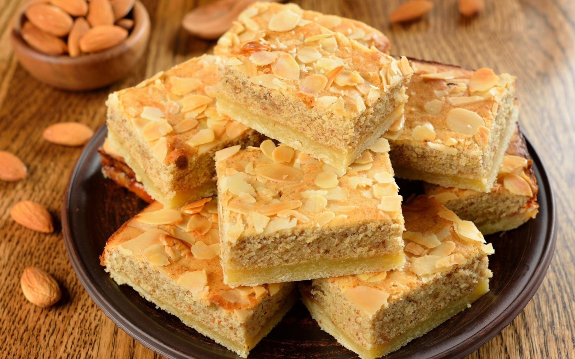 A close-up of almond pie slices elegantly arranged on a dark plate, surrounded by scattered almonds. This vibrant image serves as a delightful HD desktop wallpaper.