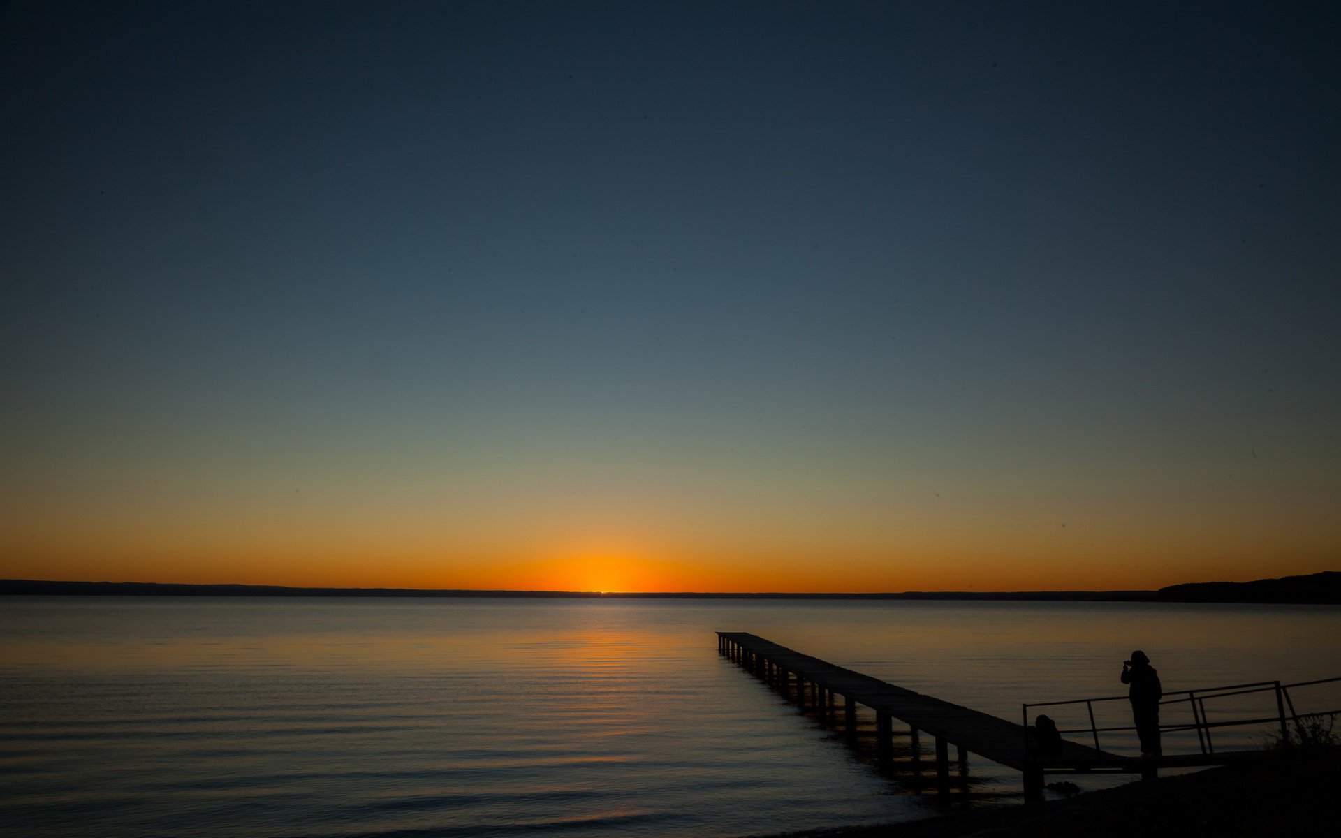 HD photography of a serene sunset over calm waters in Argentina, featuring a wooden pier extending into the lake, captured with rich colors for a desktop wallpaper background.
