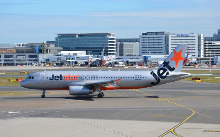 A Jetstar Airbus A320 taxiing at an airport, with modern buildings and other aircraft in the background, showcasing a vibrant travel atmosphere.